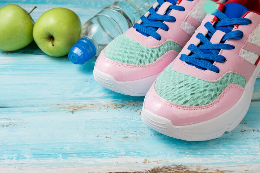 Pink sports shoes, water bottle and green apples